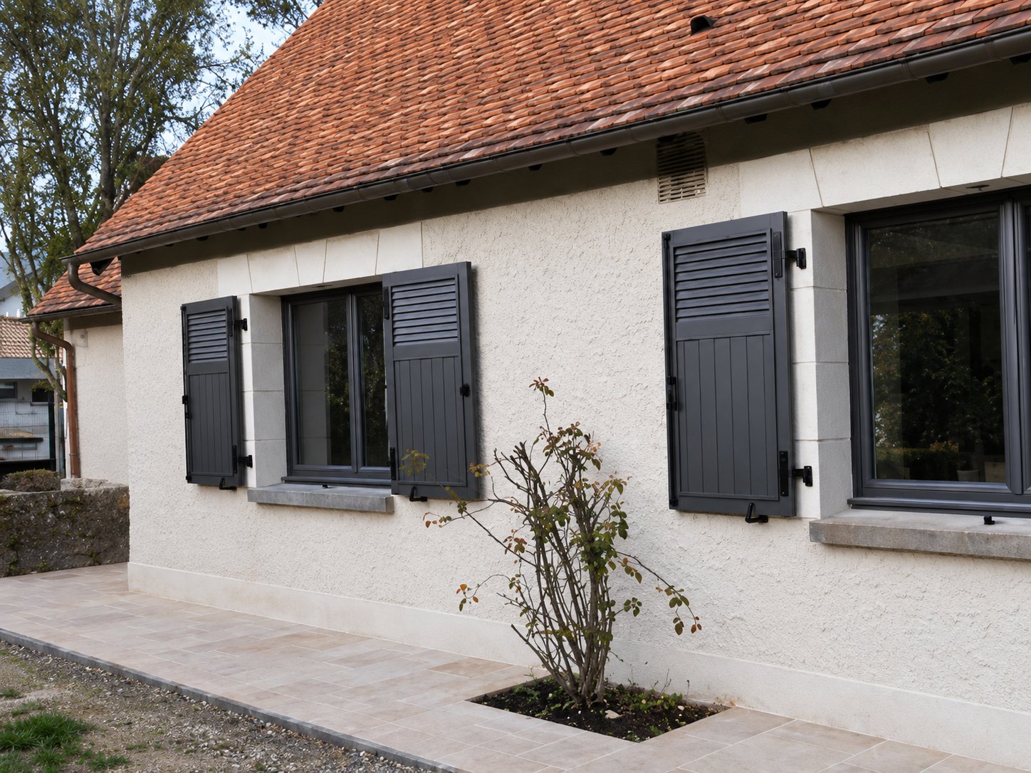 Maison rénovée avec volets gris et trottoir pavé